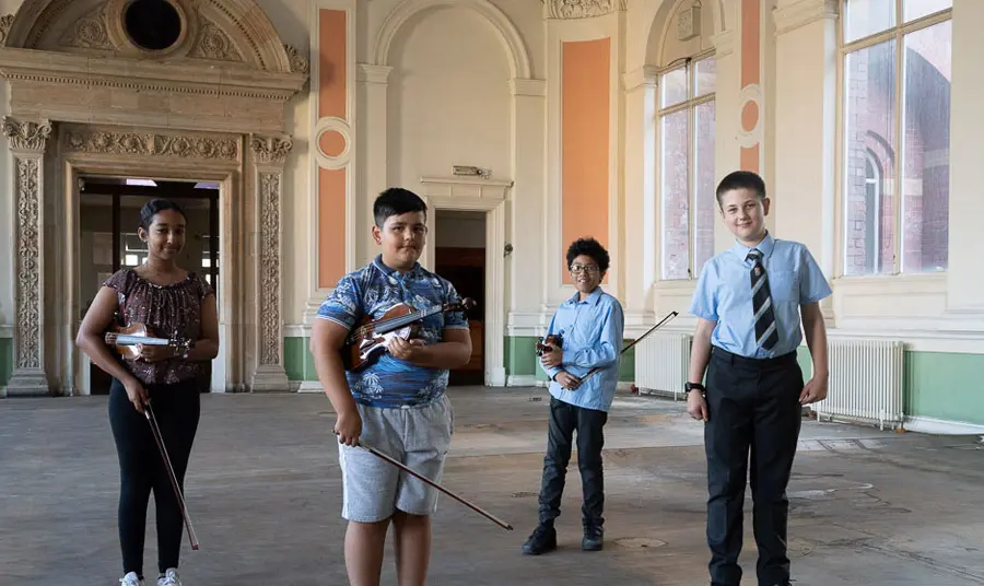Four young people holding musical instruments stand inside one of the historic rooms at Canada House