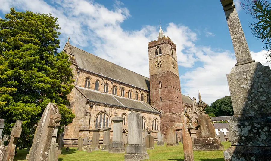 A photo of the outside of Dunblane Cathedral in Scotland. The churchyard with tombstones is in the foreground.