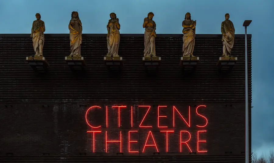 A view of the facade of the theatre, with a group of five illuminated caryatids positioned on the room above neon lettering of Citizens Theatre.