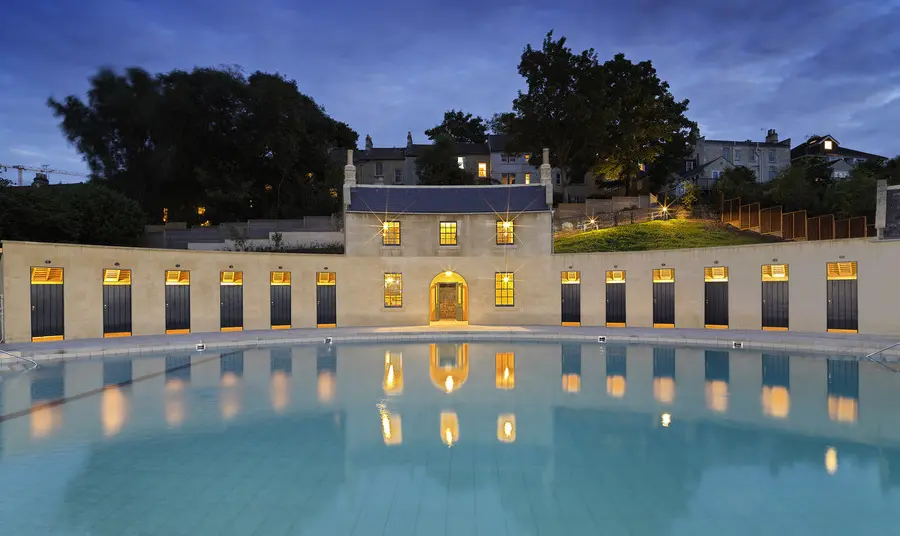 Cleveland Pools in Bath with windows lit up at night and reflections on the pool. The building is shaped like a minature Georgian crescent.