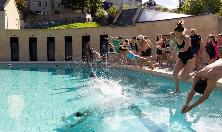 People diving into Cleveland Pools in Bath. It is an outdoor swimming pool with buildings in the shape of a miniature Georgian crescent.