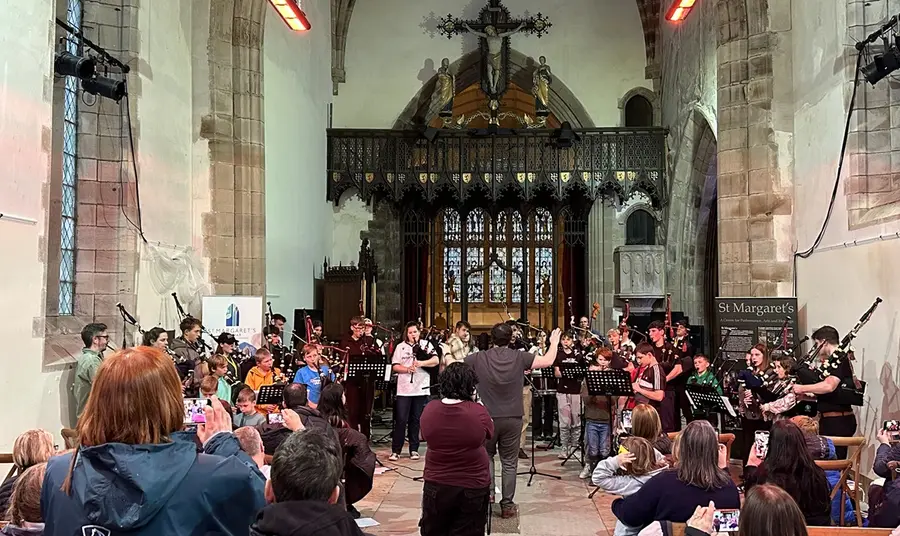 A concert taking place inside the church. Inside the church's historic interior, a small orchestra are led in a performance by a conductor, as an audience watch on.
