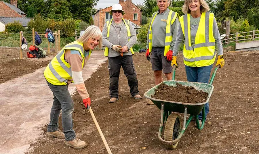 Cotswold Canals Connected Volunteers with a rake and wheelbarrow working on the new towpath at Fromebridge.