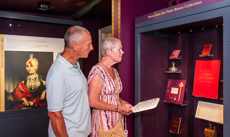 Two people looking at a museum display. There is a portrait of Duleep Singh on the wall behind them.