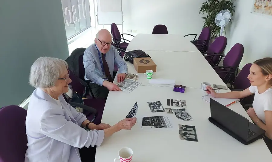 Relatives of famous sports people from Leeds are contributing to the project. Three people sit around a long office table. To the left, an older man and woman look over black and white photographs. On the right, a younger woman uses a laptop to take notes.