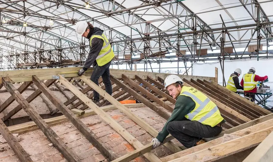 People in high visibility jackets and hard hats putting together framing for a roof