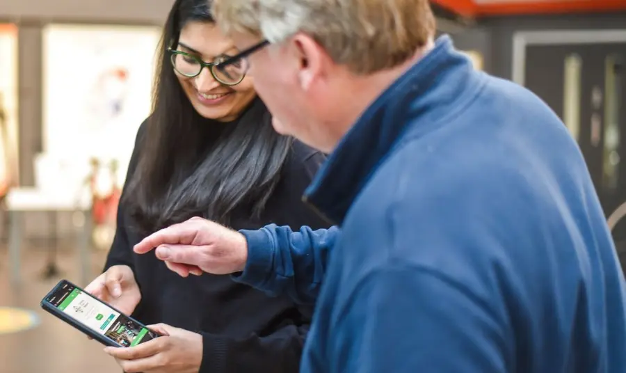 A young woman holding a mobile phone, demonstrating how to use an app to an older man