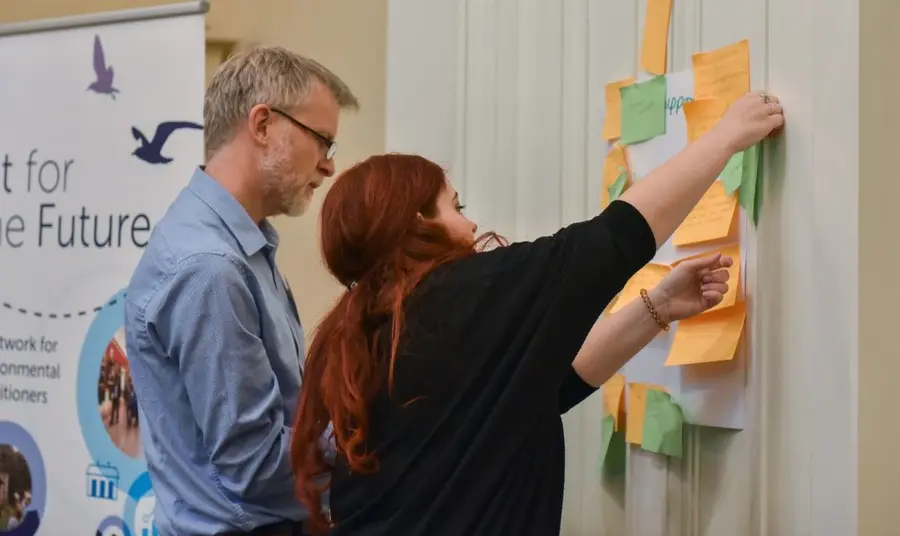 Two people sticking post-it notes on a wall as part of a collaborative workshop