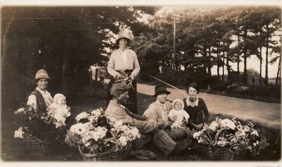 A historic black and white photograph of a group of Traveller people with infants selling flowers