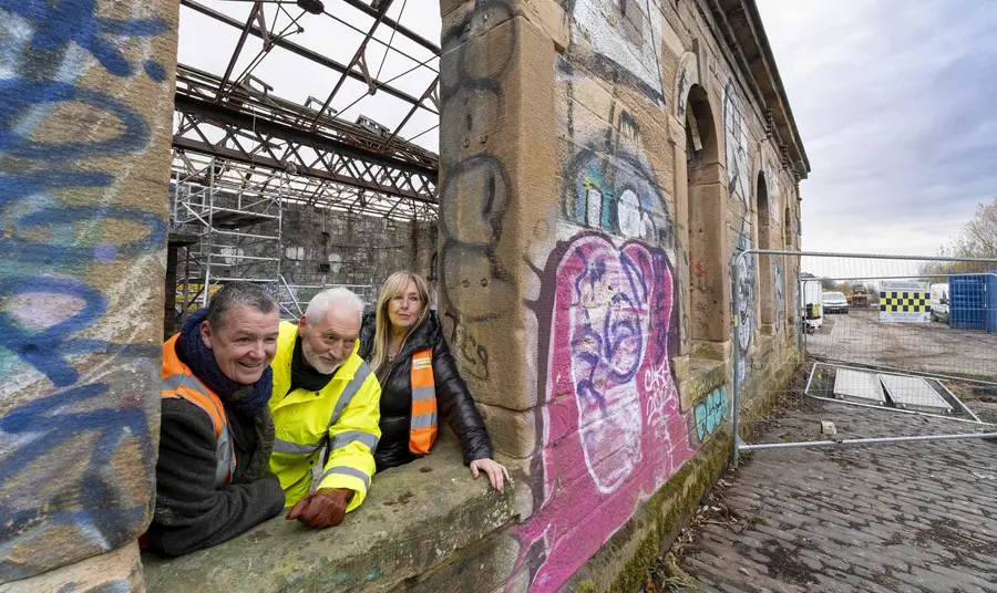Three people in high vis jackets lean out of an open window frame of the derelict Pump House at Govan Graving Docks.