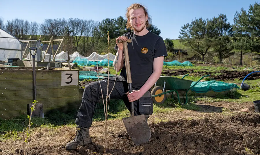 A man holding a shovel kneeling in front of a garden bed