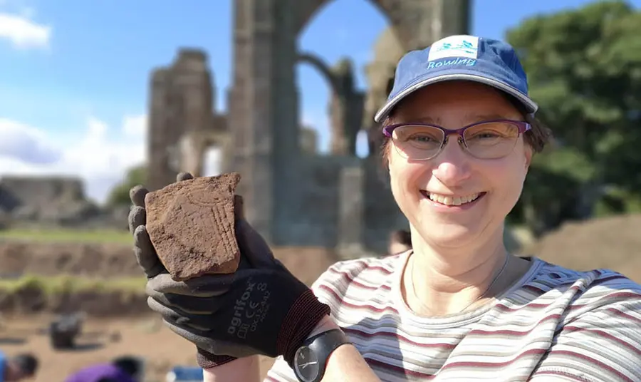 A person at an archeological dig site holds up a piece of stone which has been excavated