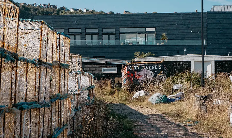 A wooden boat and fishing nets on a sandy path leading to Hastings Contemporary, a large black-clad modern building 