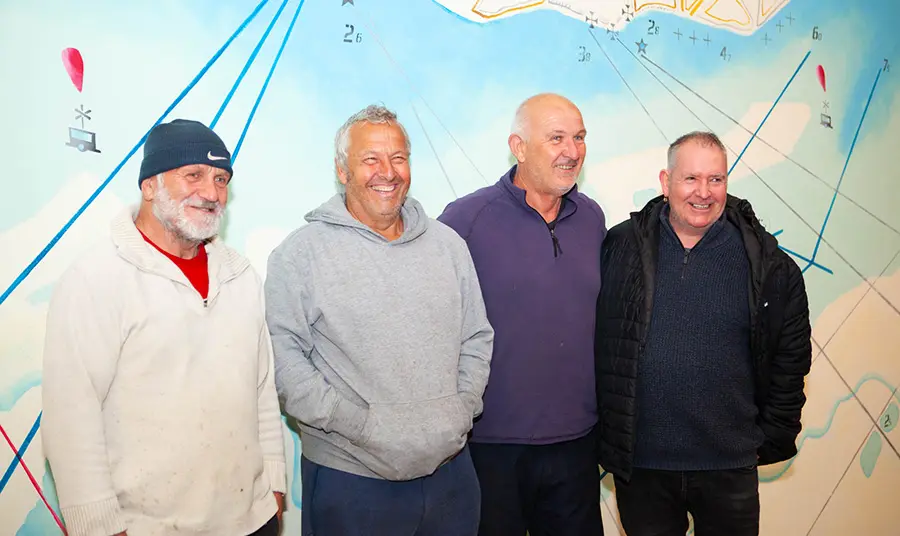 Four fishermen smiling in front of a mural of a map