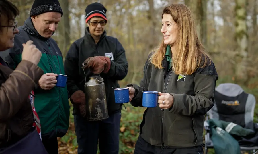 A person handing out coffee to people in a camp in the woods. Credit: Sam Frost