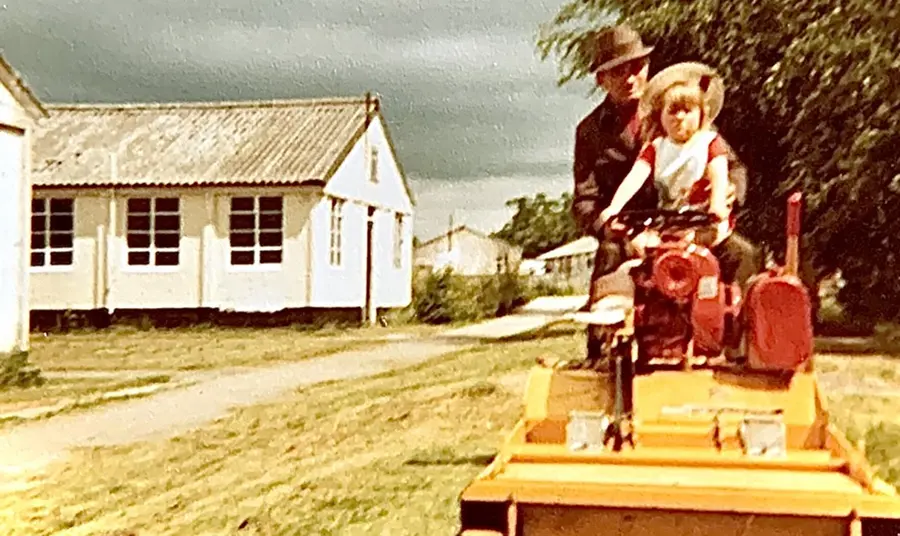 An old photograph of an adult and a child on a ride-on lawnmower