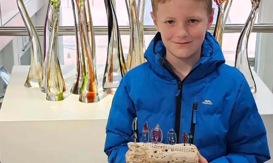 A young person holds their artwork as part of the exhibition.