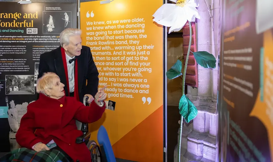 An elderly couple, smartly dressed, explore the exhibition displays together.