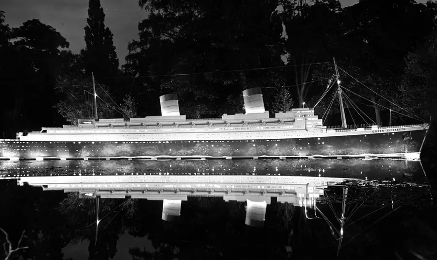 An illuminated replica of the ship Queen Elizabeth floats on the park lake at night.