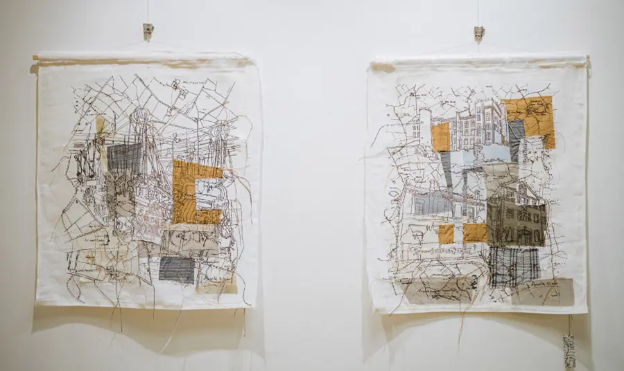 Two linen-based artworks, white and orange with map-style detailing on a white wall