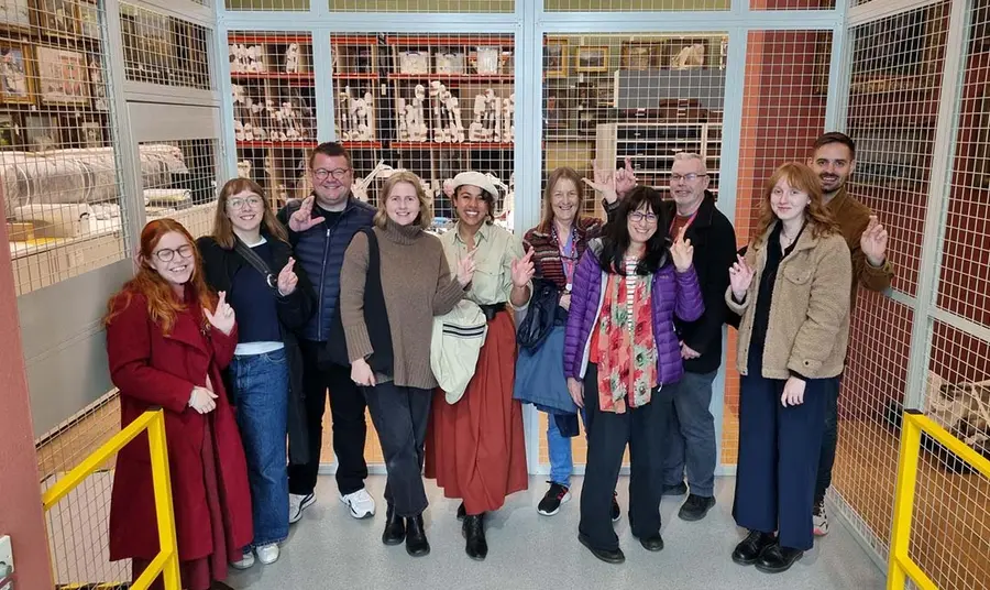 A group of people stand in Manchester Art Gallery doing the crossed fingers.