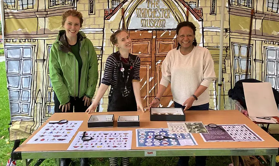 Three people at an event stand with information about insects