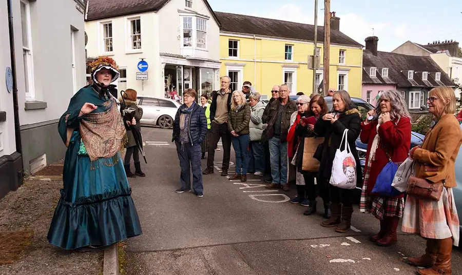 A person in historical dress stands in a street and talks to a tour group
