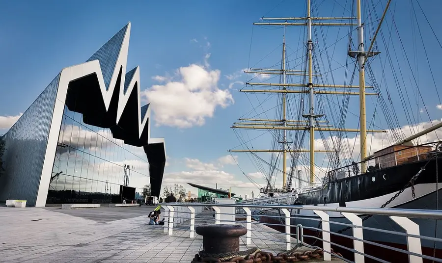 A view of the facade of the Riverside Museum in Glasgow, opposite a docked tall ship in the Clyde.