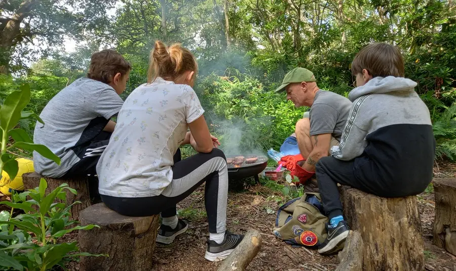 A group of young people engage in outdoor activities Group of young people sat around a campfire in a wood