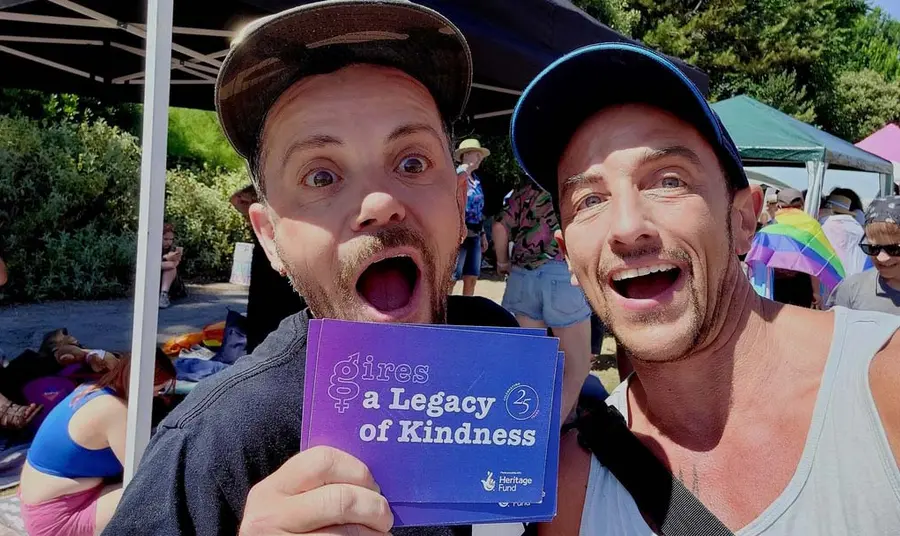 Two people at an outdoor event holding a card saying A Legacy of Kindness