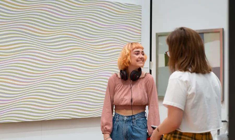 Two Gallery visitors in front of a Bridget Riley patterned painting