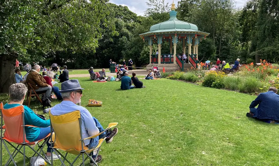 People sitting in a sunny park, near a bandstand