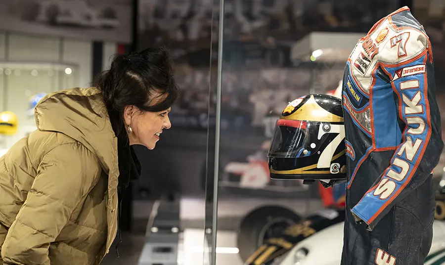 Woman looking into a glass case displaying Barry Sheene's racing leathers and helmet