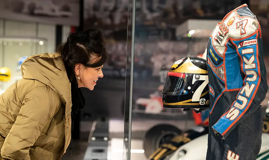 Woman looking into a glass case displaying Barry Sheene's racing leathers and helmet