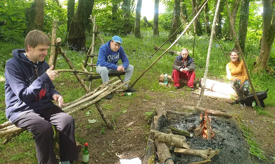Grantiau cymunedol yn rhoi hwb i lesiant ledled Cymru People chat round a campfire in woodland