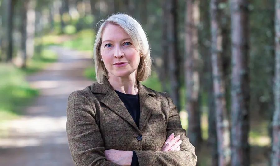 Person stands in nature with arms crossed, looking at camera