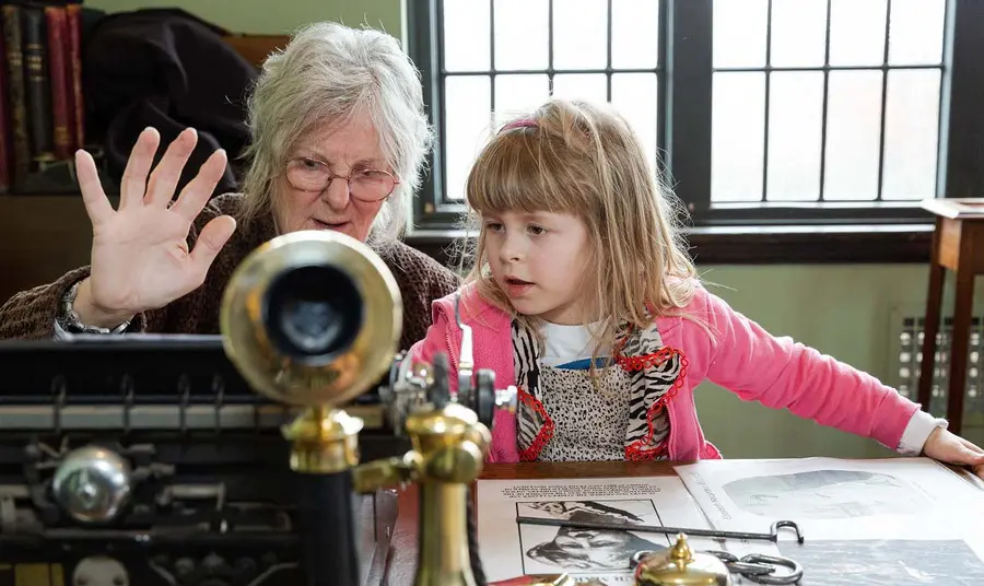 A person teaching a young child about past events and showing them an old type writer