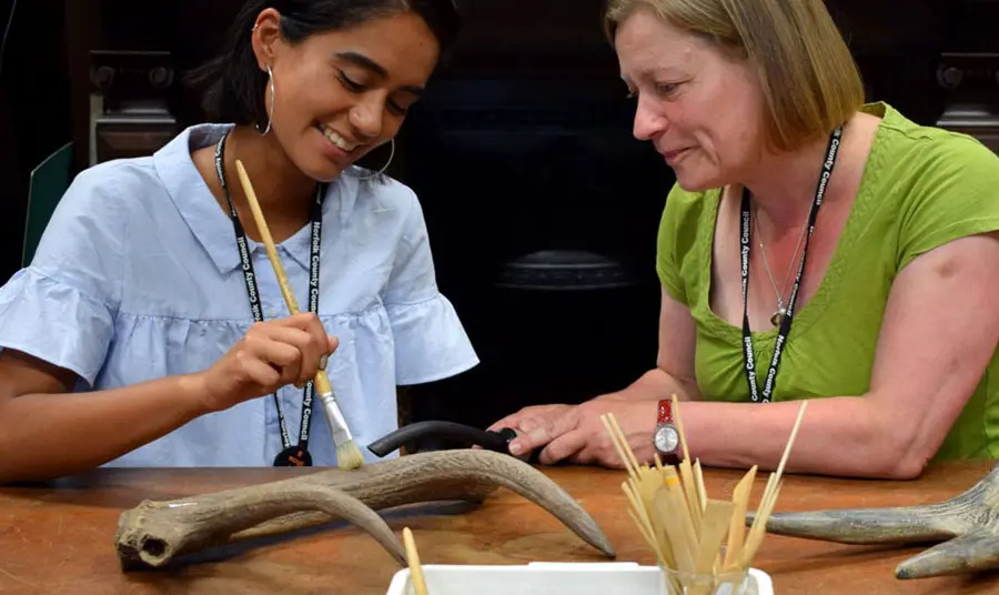 A woman watching as a younger woman cleans an antler behind the scenes at Norfolk Museums