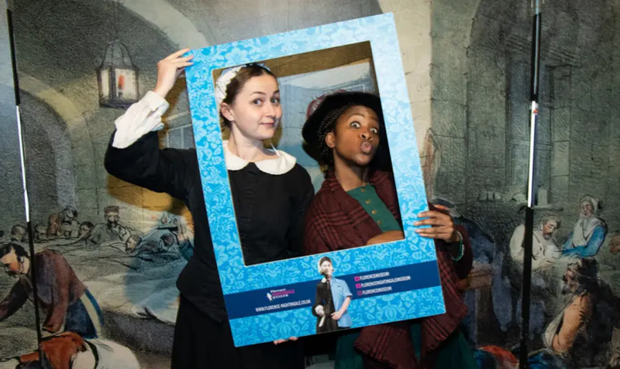 Image of two people in historic nursing outfits depicting Mary Seacole and Florence Nightingale, holding a frame to their faces
