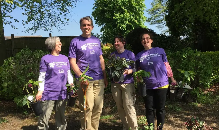 Four people holding plants whilst smiling at camera