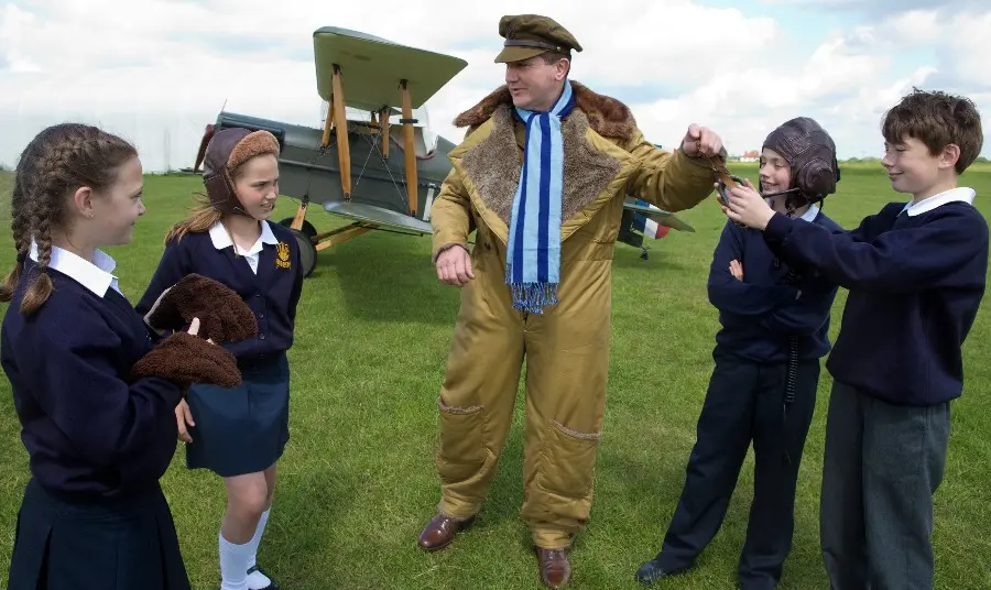 Four children with a man in First World War dress in front of a biplane