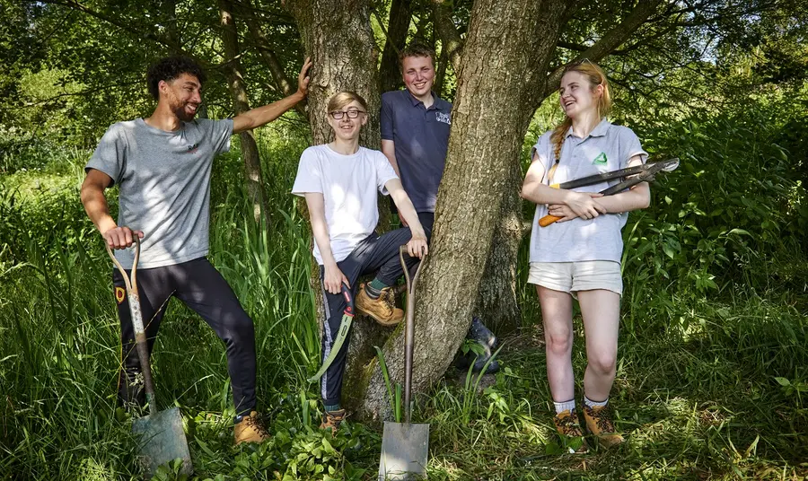 Young people standing in nature with gardening tools