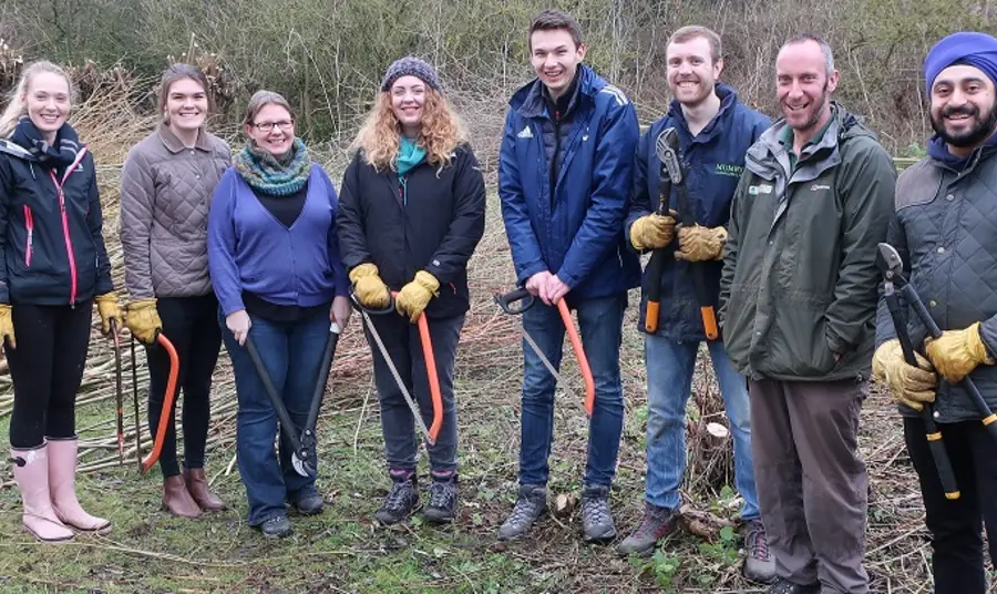 Volunteering guidance Group of people holding tools outdoors, looking towards camera and smiling