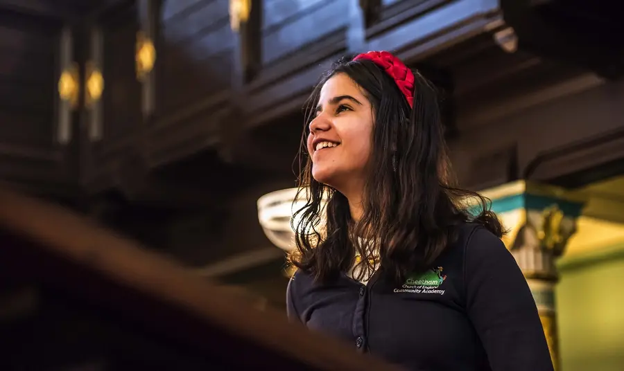  A young child in a school uniform looking up and smiling inside a synagogue 