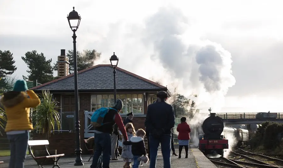 Family gathered on the platform at Whitehead Railway station watching a locomotive approach