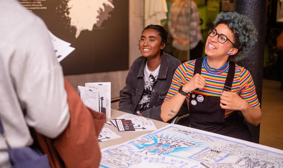 Young people talking at an event stall with posters and leaflets.