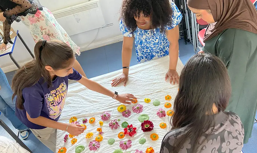 A group of young people arranging flowers and leaves on a white sheet