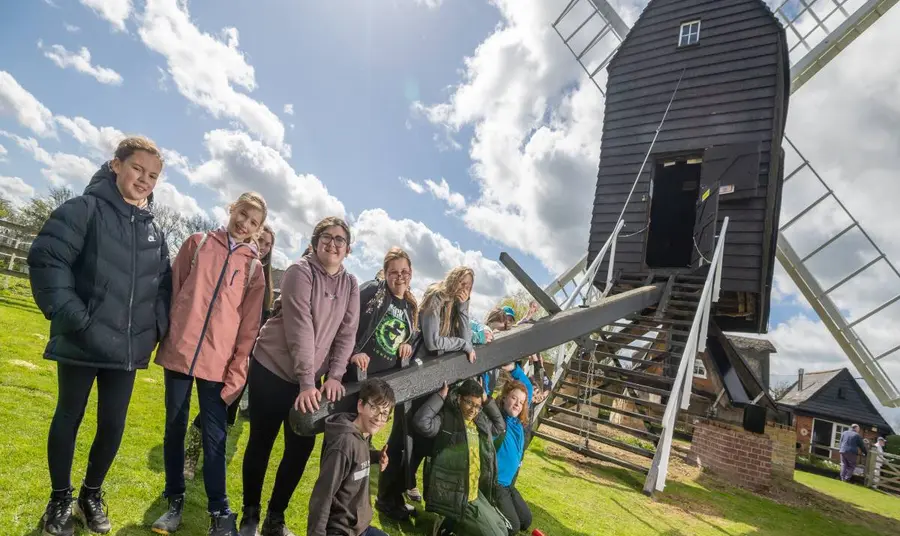 A group of children leading on a piece of wood attached to a windmill.
