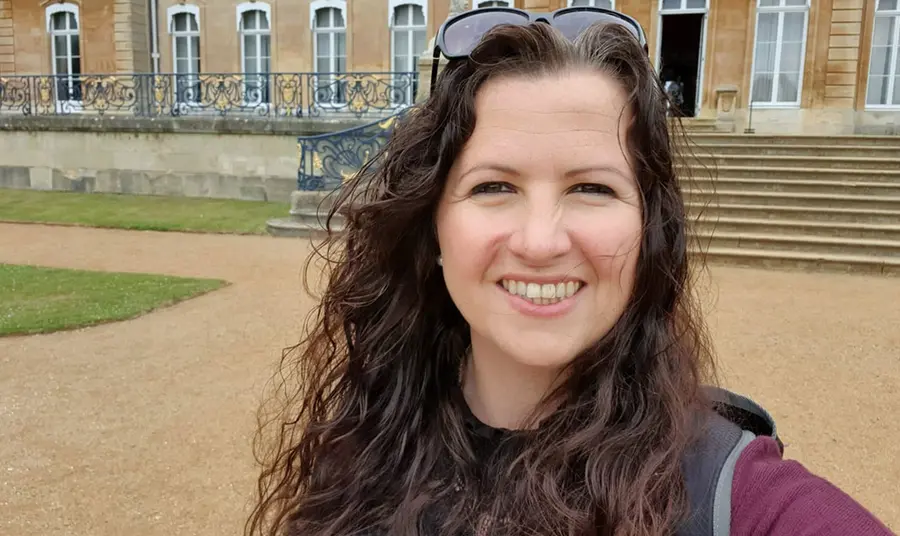 Selfie of a women with long dark hair standing in front of a historic house