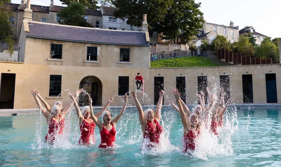 A group of swimmers in red swimsuits jumping out of the water at Cleveland Pools